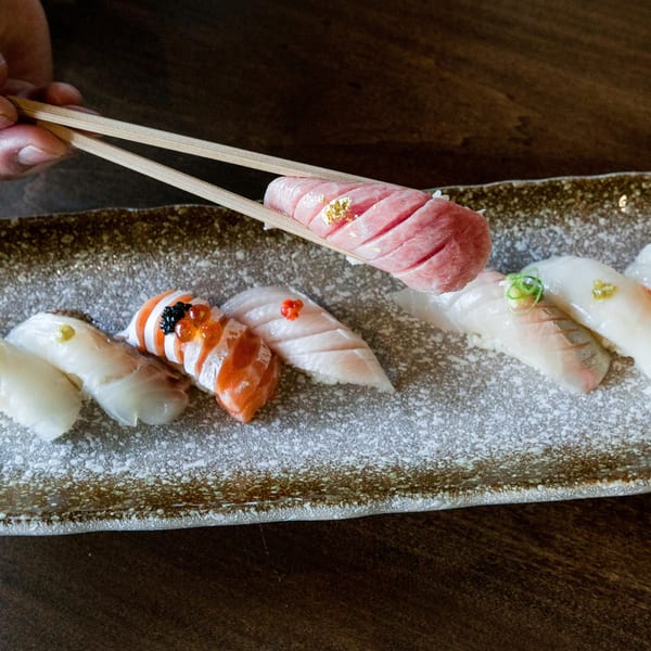 Chopsticks holding a piece of Izakaya Tora's tuna sushi with gold flakes above a sushi platter.