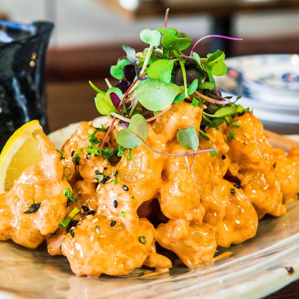 Izakaya Tora's crispy shrimp in spicy mayo, garnished with microgreens, sesame seeds, and a lemon wedge.