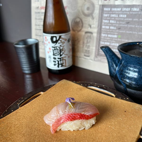 Izakaya Tora's sushi with two slices of fish on rice, garnished with a purple flower.