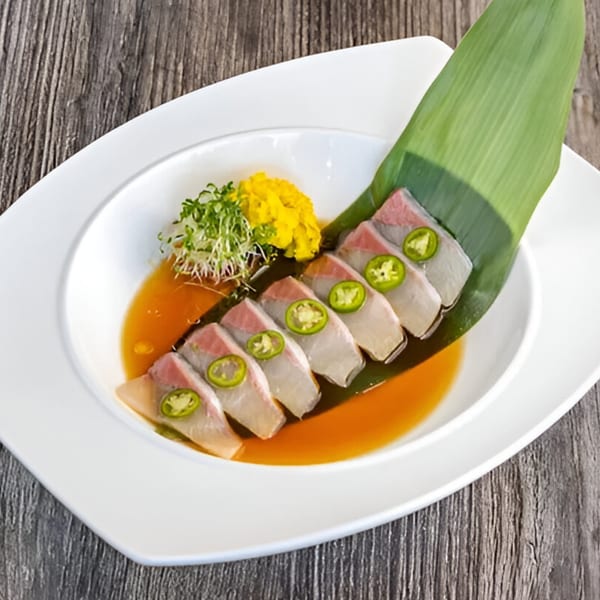 Izakaya Tora's yellowtail sashimi with jalapeño slices, microgreens, and yellow garnish in ponzu sauce.